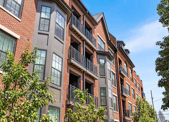 A red brick building with balconies and trees in front.
