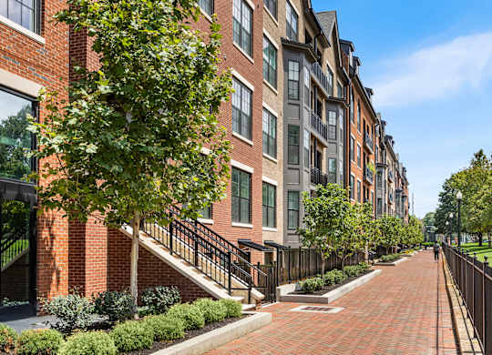 A long brick walkway leads to a building with a black fence on one side.