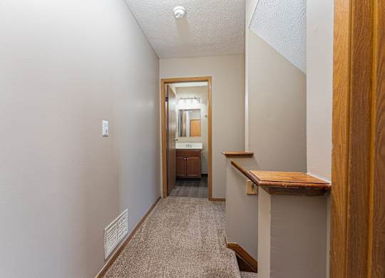 A hallway with a carpeted floor and a wooden railing on the right side.