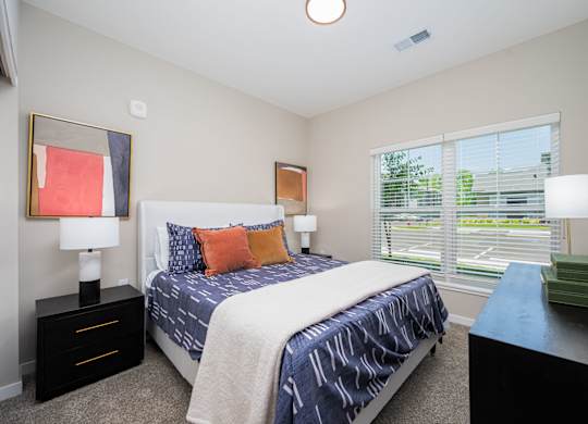 A bedroom with a bed, nightstands, and a window with blinds.