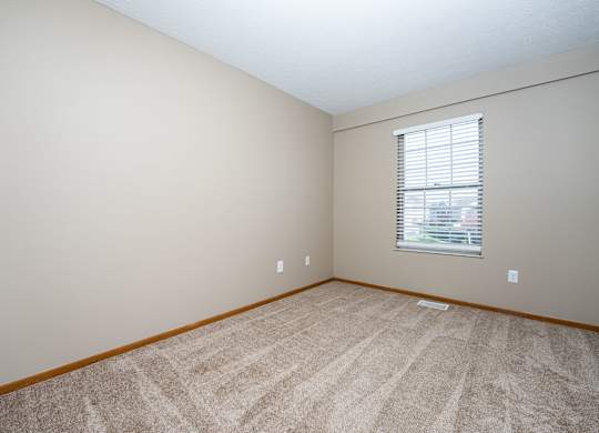 A room with a carpeted floor and a window with blinds