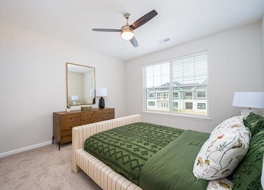 A bedroom with a bed, dresser, mirror, and window.