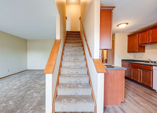 an empty living room with stairs leading up to a kitchen