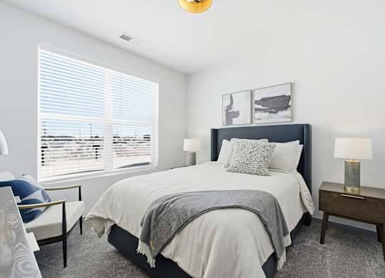 A bedroom with a large bed and a window with blinds.