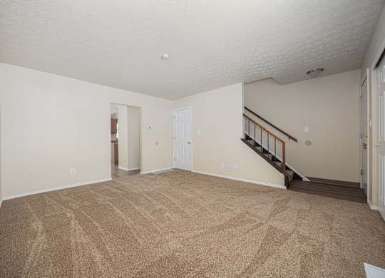 A room with a carpeted floor and a staircase.