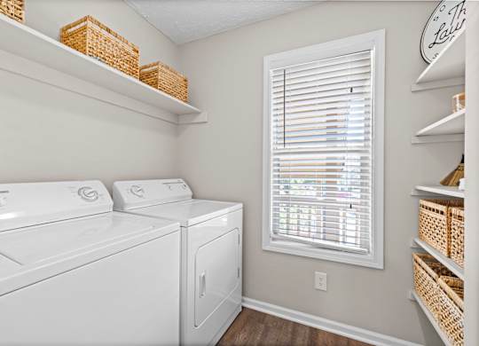 A laundry room with a washer and dryer and a window with blinds.