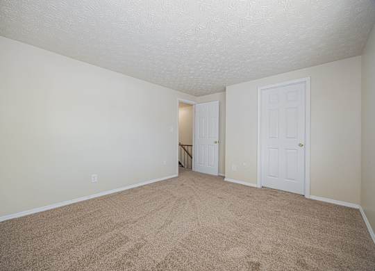 A room with carpeted floor and two doors.