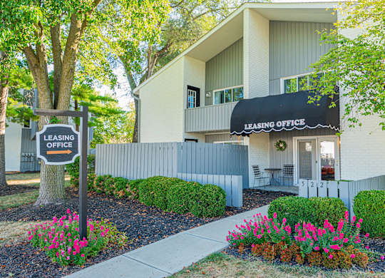 the front of a building with a leasing office sign and flowers