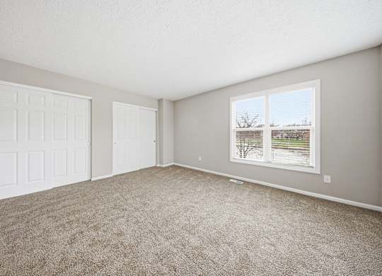 A room with a carpeted floor and a window showing a view of trees and a building.