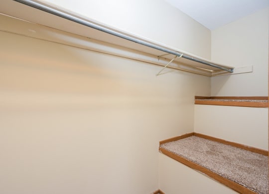 a walk in closet with a white wall and a shelf on the wall