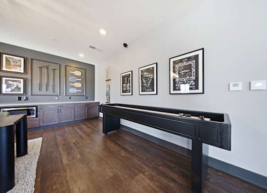 A pool table in a room with a wooden floor and framed pictures on the wall.