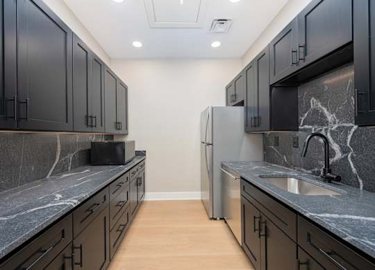 A kitchen with black cabinets and a marble counter top.