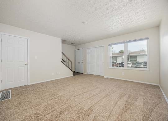 A room with a carpeted floor and a window showing a view of other buildings.