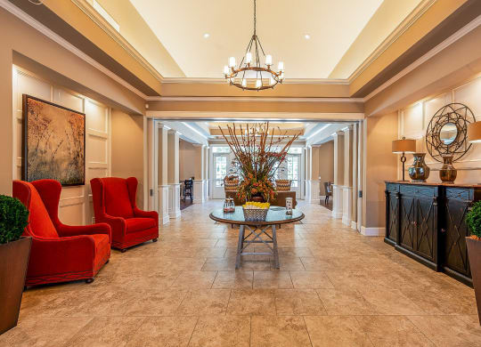 a lobby with red chairs and a table and a chandelier