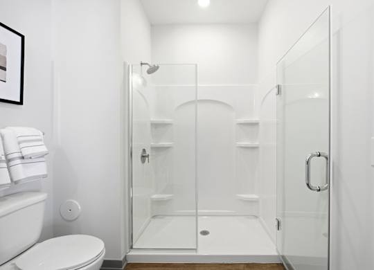 A white bathroom with a toilet, a glass shower door, and a white towel.