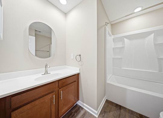 A white bathroom with a round mirror and a white bathtub.