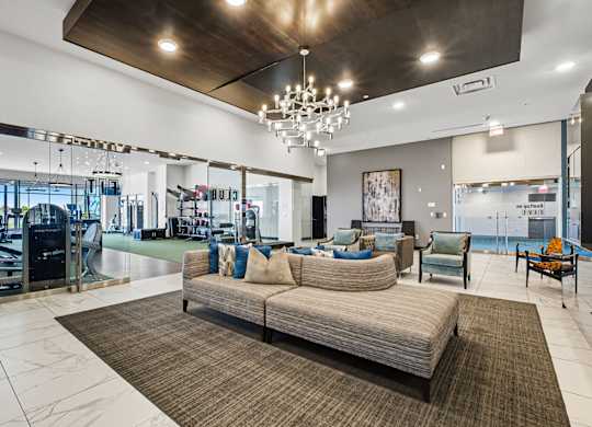 A large, modern living room with a couch, chairs, and a gym in the background.