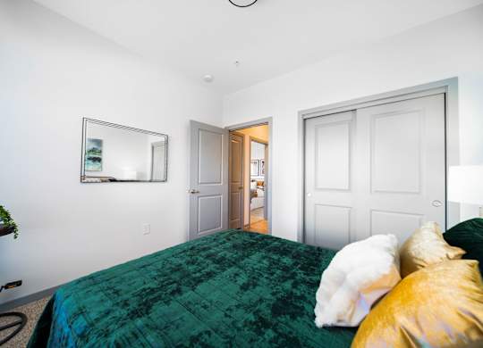 A bedroom with a green bedspread and a white dog on the bed.