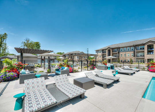 A sunny day at a poolside with lounge chairs and a building in the background.