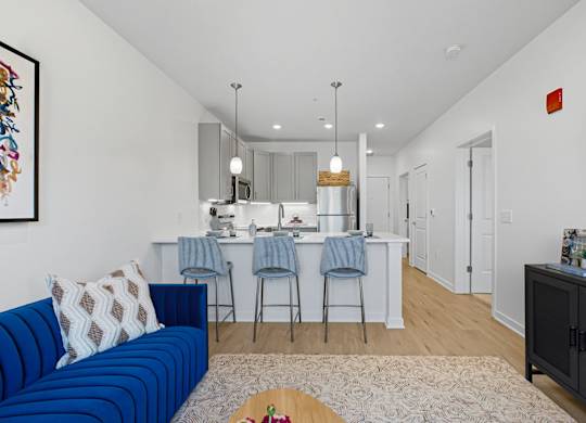 A blue couch sits in a living room with a kitchen in the background.