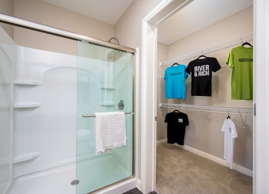 a walk in closet with a glass shower and shirts hanging on the wall