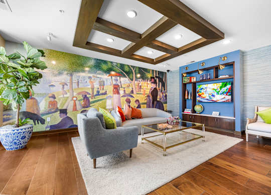 A living room with a grey sofa, a white armchair, a coffee table, and a large mural on the wall.