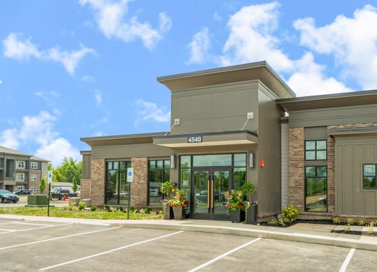 the front of a building with glass doors and a parking lot
