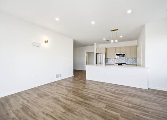 A room with wooden floors and a kitchen area in the background.