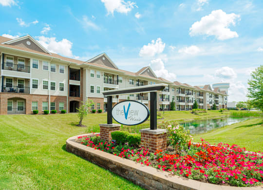 an apartment building with a sign in front of a pond and flowers