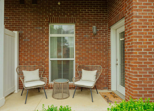 a patio with two chairs and a table in front of a brick house