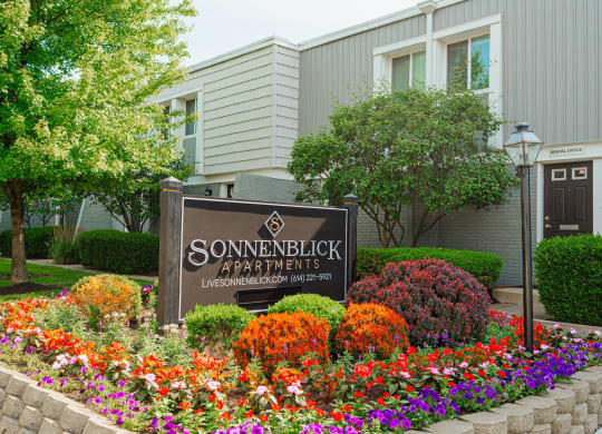 a sign in front of a garden of flowers and a building
