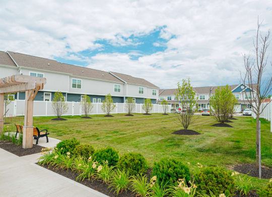 a park with a lawn and benches in front of a row of houses