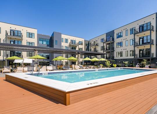 A pool surrounded by wooden deck and buildings.