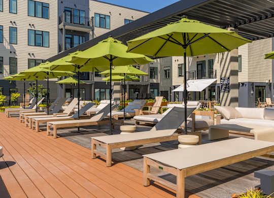 A row of lounge chairs and tables are set up on a wooden deck.