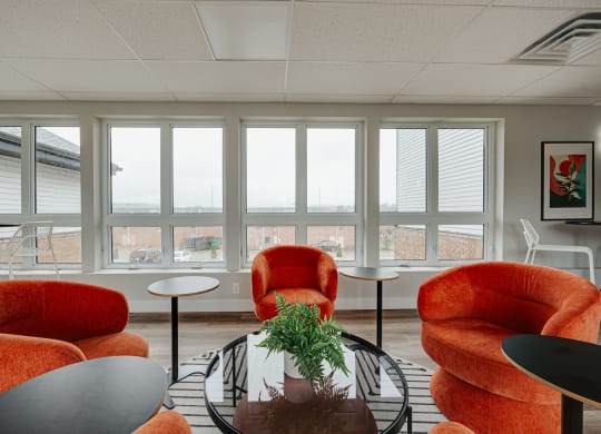 a living room with orange chairs and a table and windows