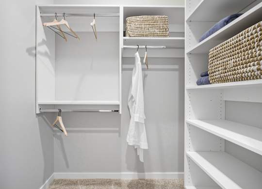 A white closet with clothes hanging and baskets on the shelves.