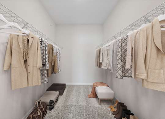 A walk in closet with clothes hanging and a bench.
