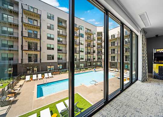 A view from inside a building looking out to a pool and sun loungers.