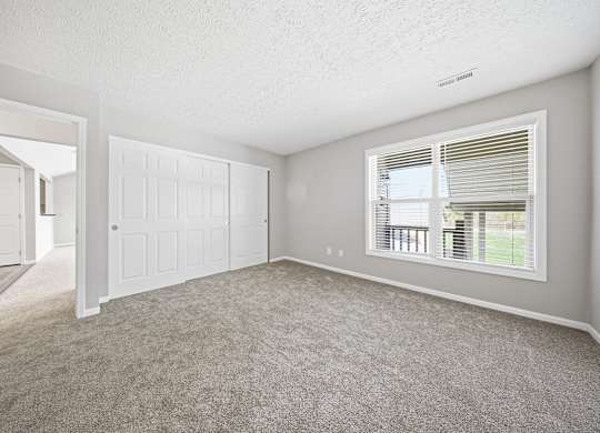 A room with a carpeted floor and a window with blinds.