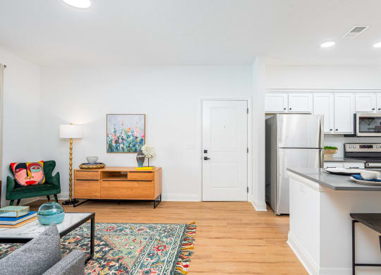 a living room with a kitchen with a refrigerator and a microwave