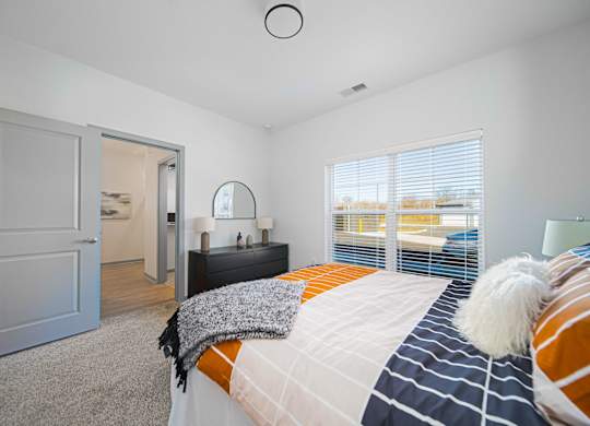 A bedroom with a bed, a nightstand, and a window with blinds.