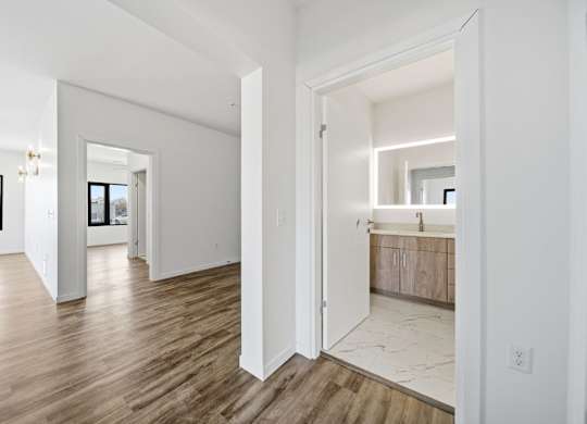 A room with white walls and wooden flooring with a doorway leading to another room.