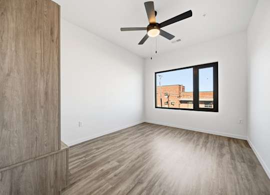 A room with a ceiling fan and a window showing a building outside.