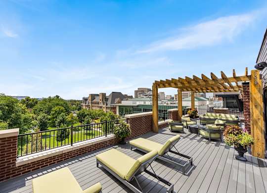 A wooden deck with a pergola and lounge chairs overlooks a cityscape.