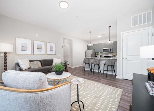A modern living room with a grey sofa and a kitchen area in the background.