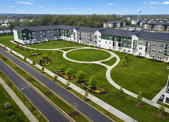A large green and white building with a circular garden in front.