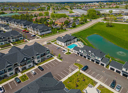 A bird's eye view of a residential area with houses, cars, and a lake.