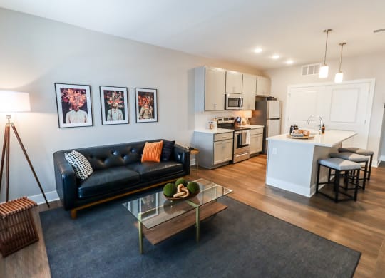 a living room with a black leather couch and a glass coffee table in front of a kitchen