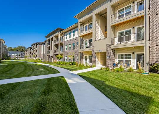 A long white pathway leads through a grassy area between two rows of apartment buildings.