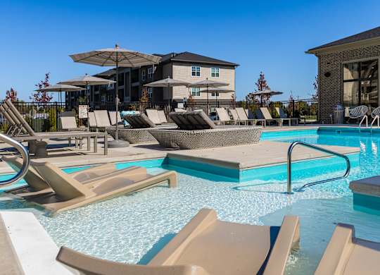 A pool with sun loungers and a building in the background.